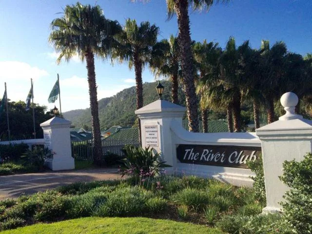 White entrance pillars and signage for The River Club estate with palm trees