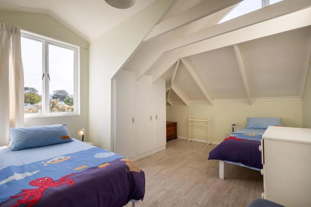 Bright attic bedroom with two beds, pitched ceiling, and garden views