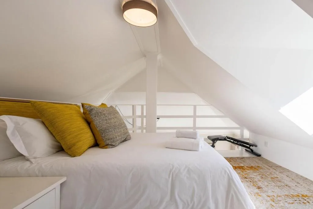 Bright attic bedroom with queen bed, yellow cushions, sloped ceiling