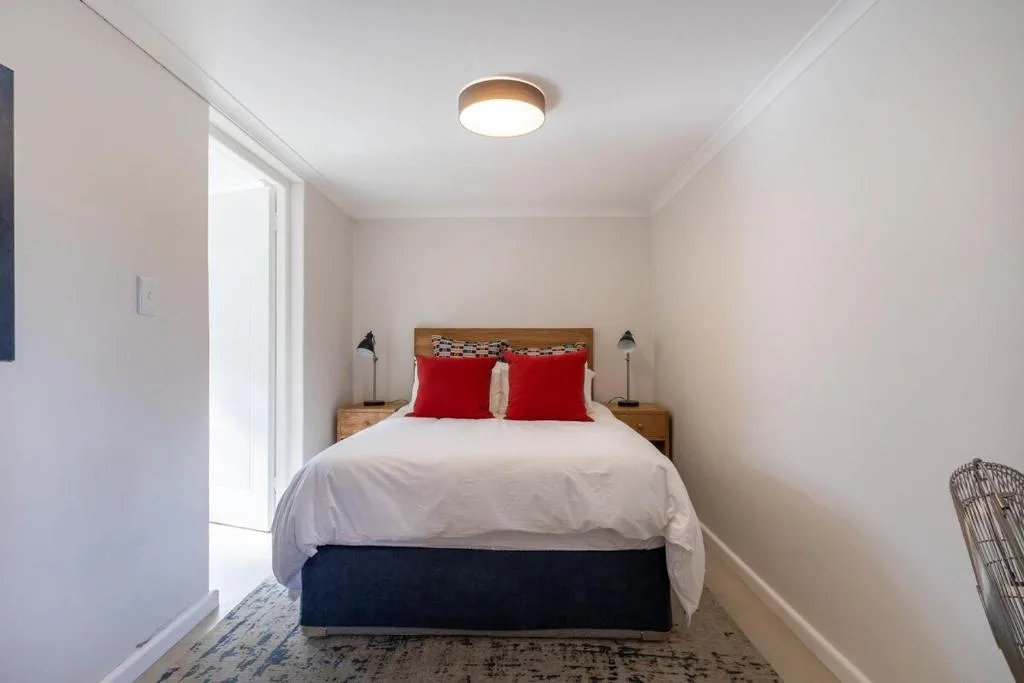 Bright bedroom with queen bed, red pillows, wooden headboard, and pendant lamps