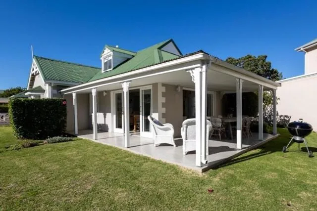 Modern cottage with green roof, white trim, and covered porch overlooking manicured lawn