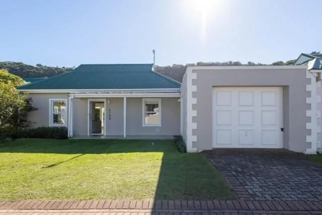 White cottage with teal roof, manicured lawn, and attached garage