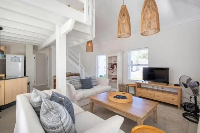 Bright open-plan lounge with white sofas, wooden furniture, and pendant lights