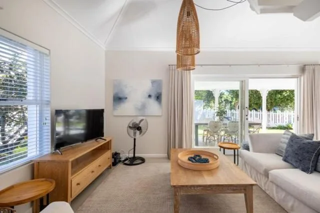 Bright lounge with sofa, wooden TV unit, and garden views through large windows