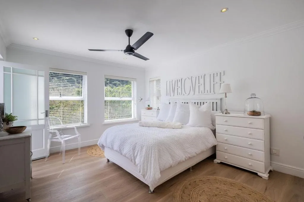Bright bedroom with queen bed, white dresser, ceiling fan, and garden views