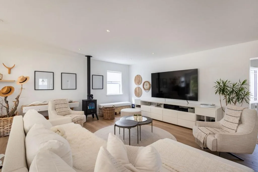 Spacious open-plan lounge with cream sofas, flat-screen TV, and wood stove
