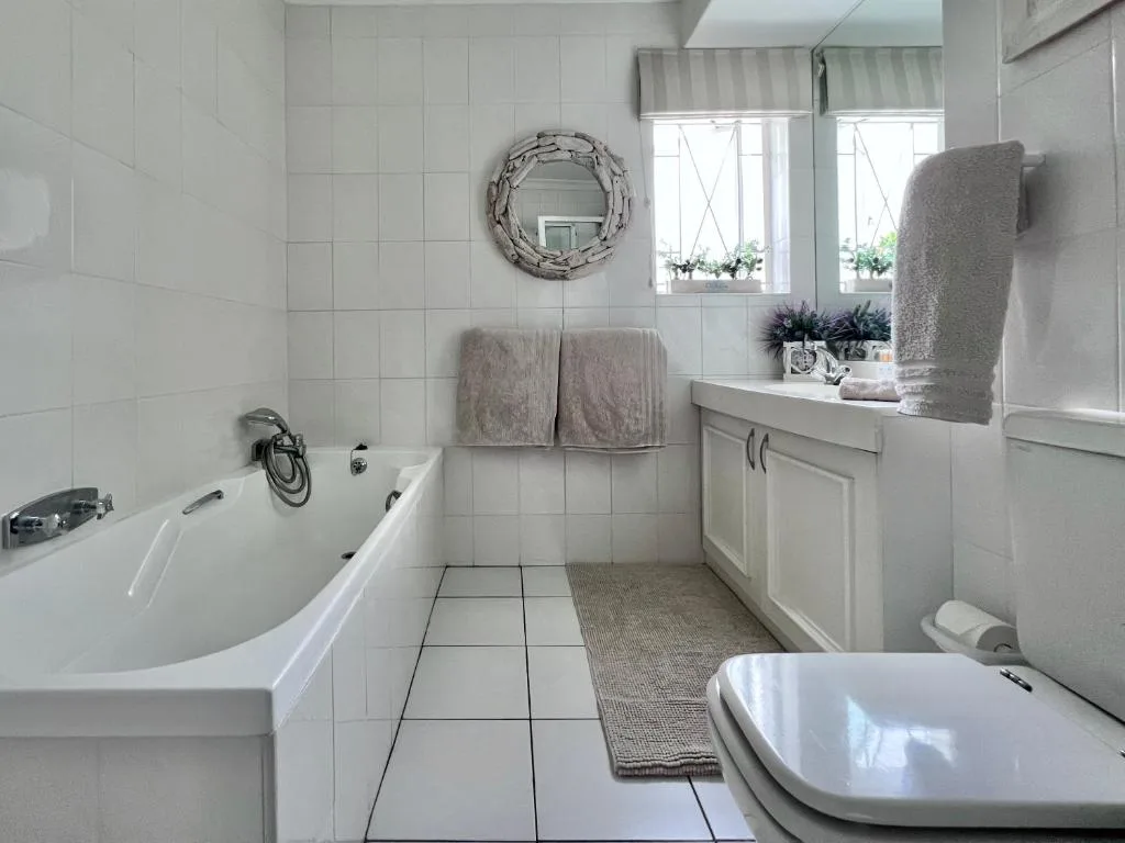 Bright bathroom with white tiles, bathtub, vanity, and decorative mirror