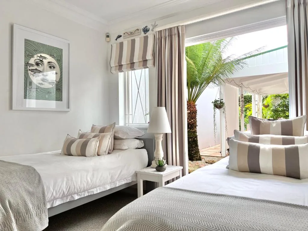 Bright bedroom with twin beds, striped pillows, and garden view access