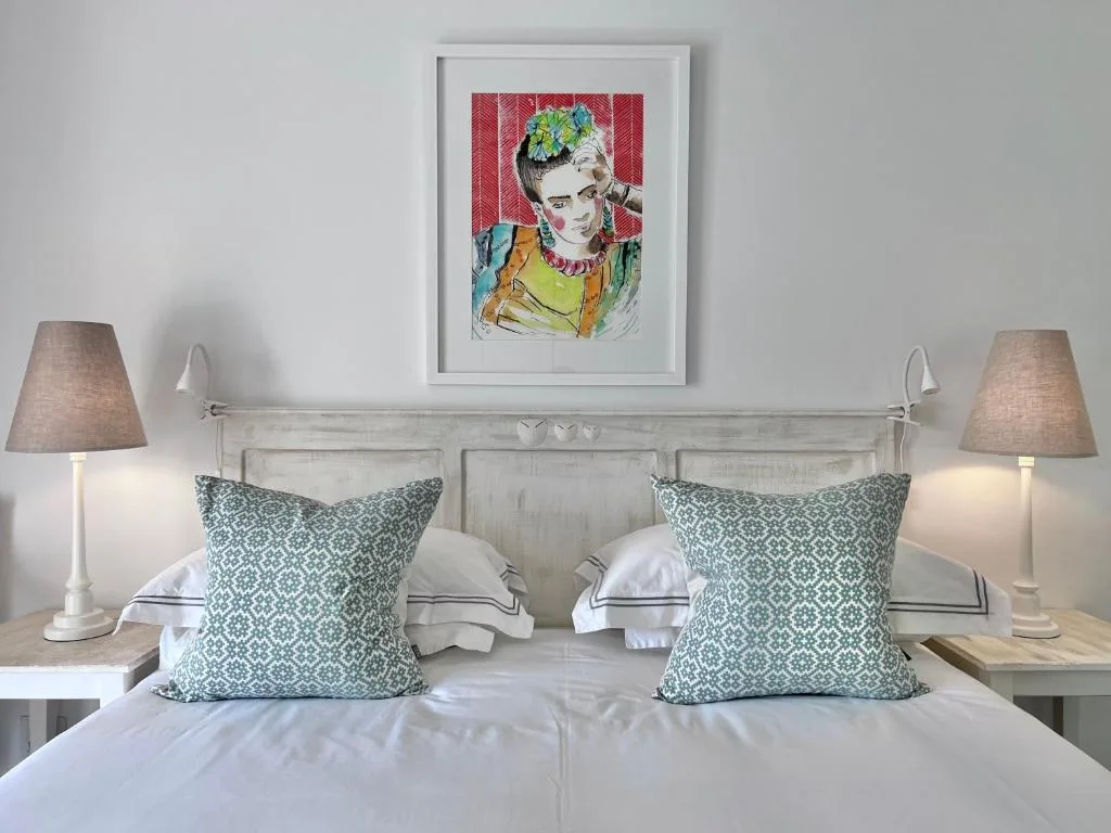 Bright bedroom with white bedhead, patterned cushions, and framed artwork