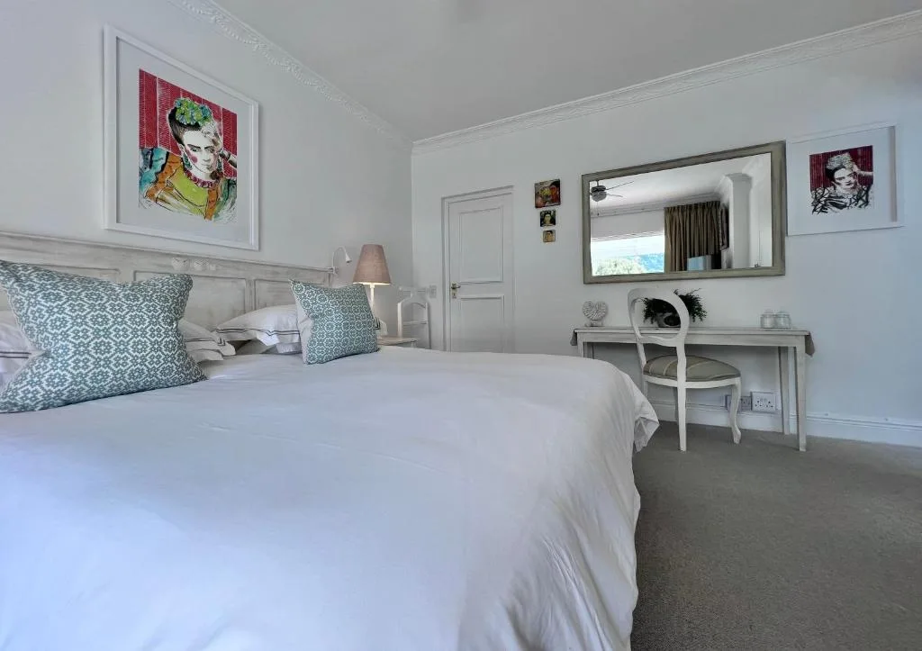 Bright modern bedroom with white bedding, patterned cushions, and vanity desk