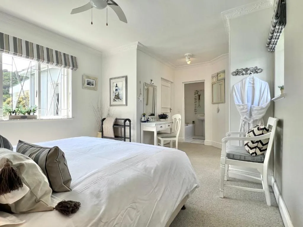 Bright bedroom with white bedding, ensuite bathroom visible, ceiling fan overhead