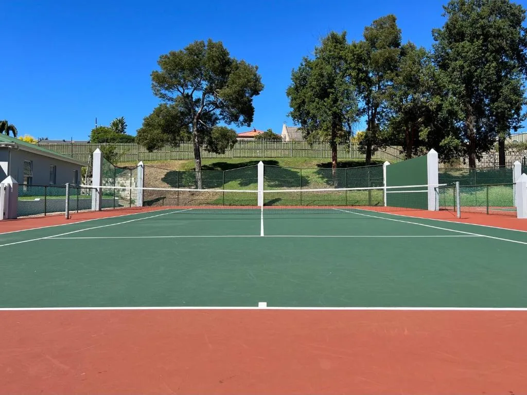 Professional tennis court with net on manicured grounds, clear blue sky