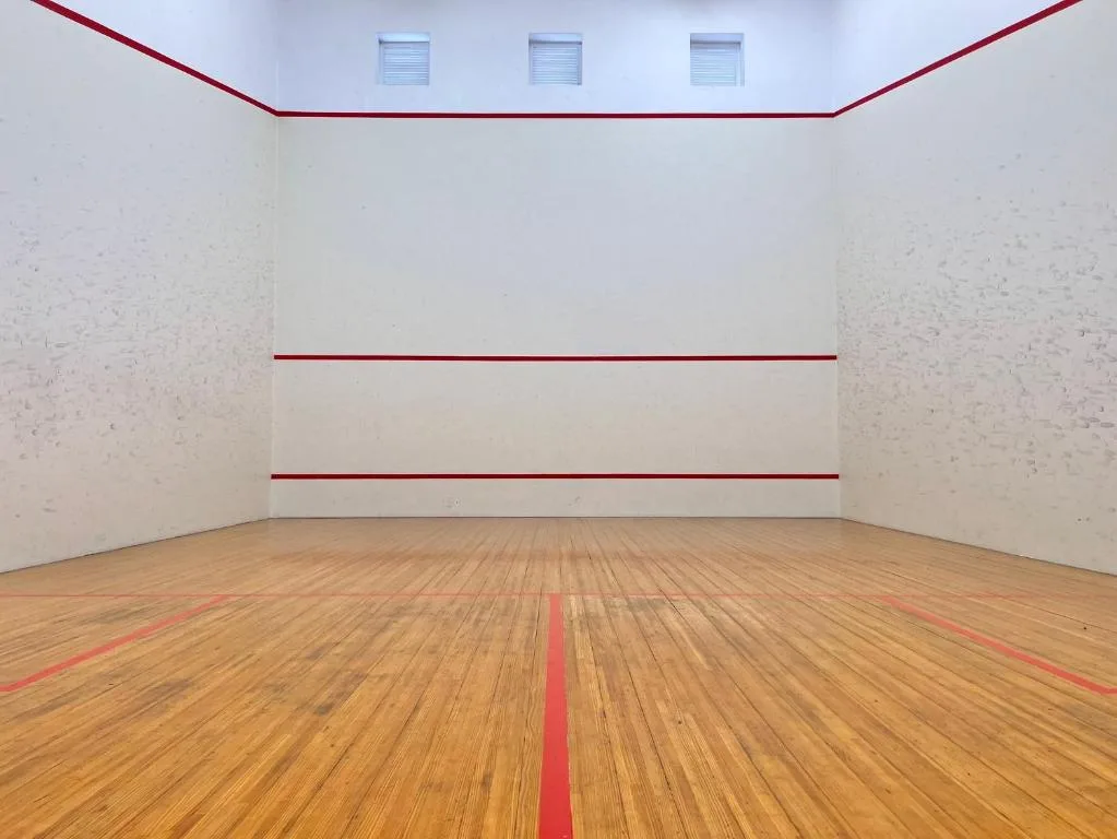 Empty indoor squash court with wooden flooring and red lines