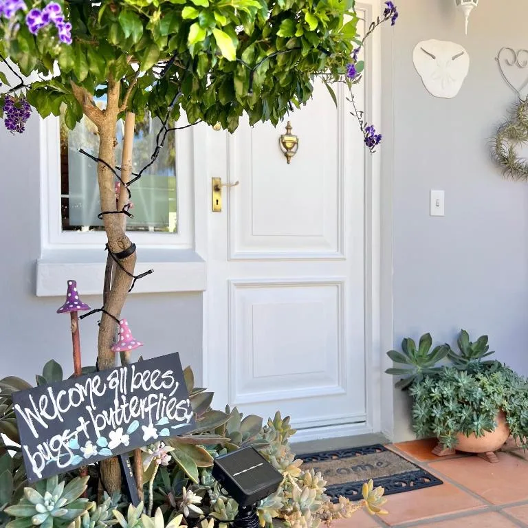 Charming entrance with white door, flowering vine, decorative welcome sign, and potted succulents