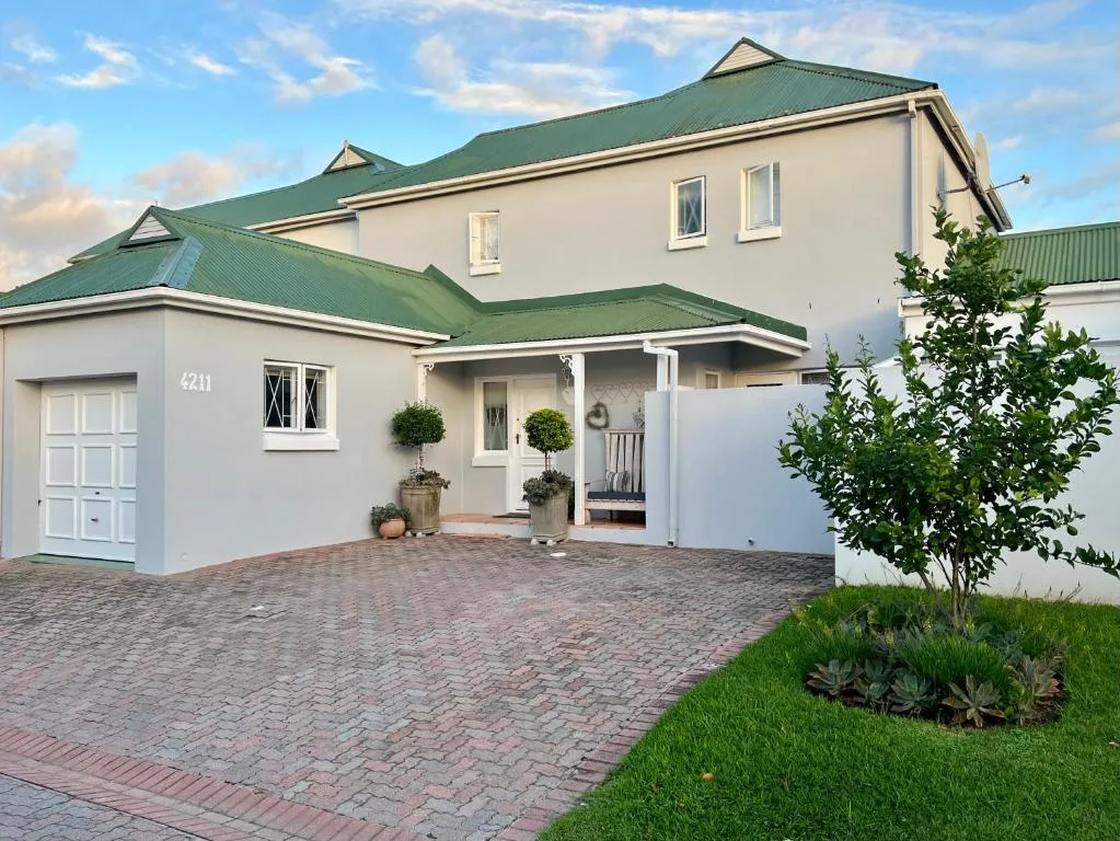 Modern white house with green roof, paved driveway, and manicured garden entrance