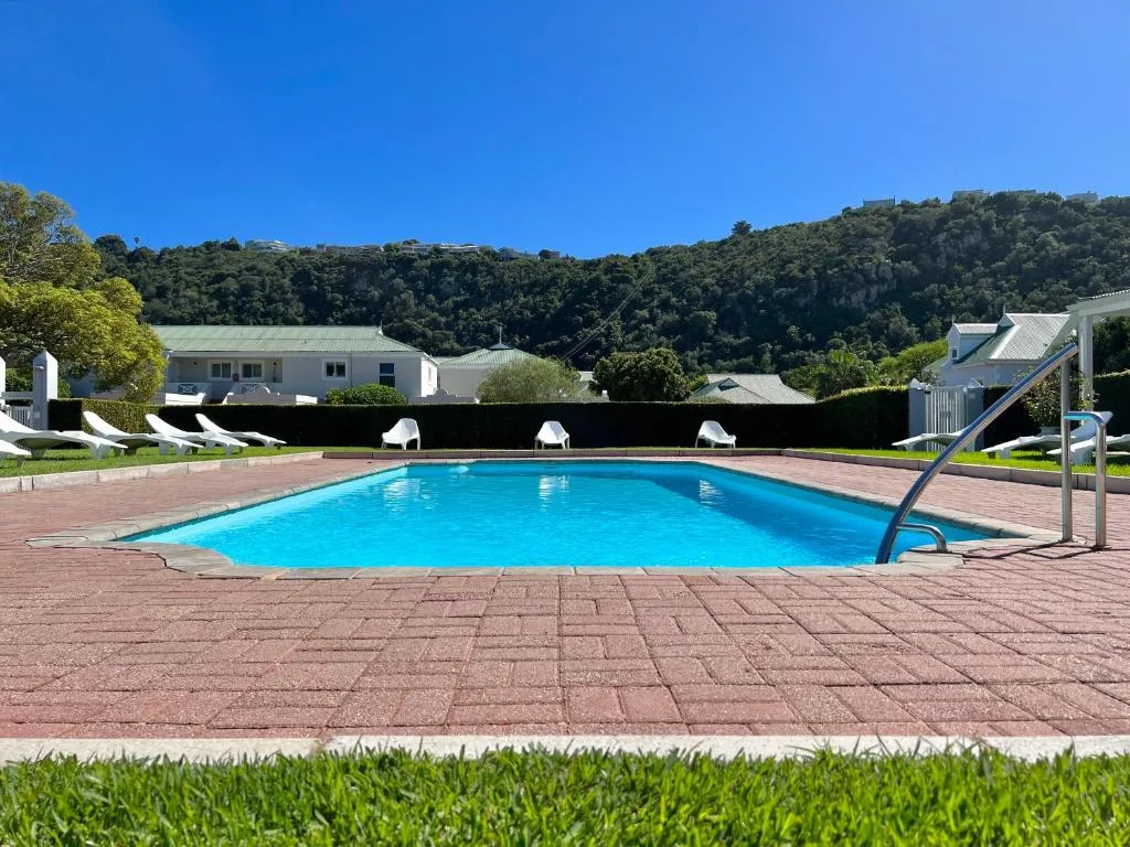 Large sparkling blue swimming pool with brick surround and forested hillside backdrop