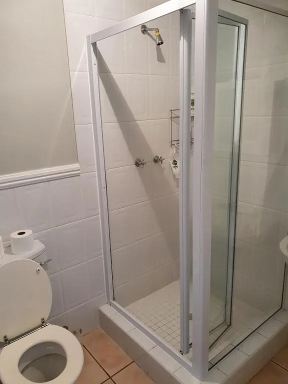 Clean white-tiled shower cubicle with glass door and toilet visible