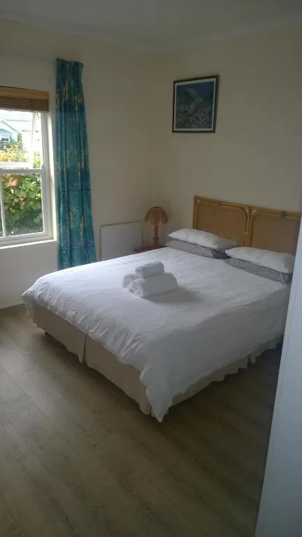 Bright bedroom with double bed, wooden headboard, fresh white linens, teal curtains