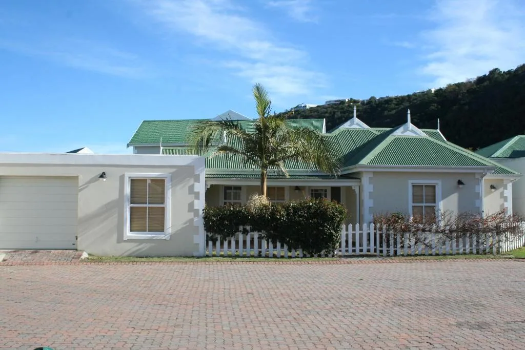 White cottage with green roof and white picket fence, palm tree in front