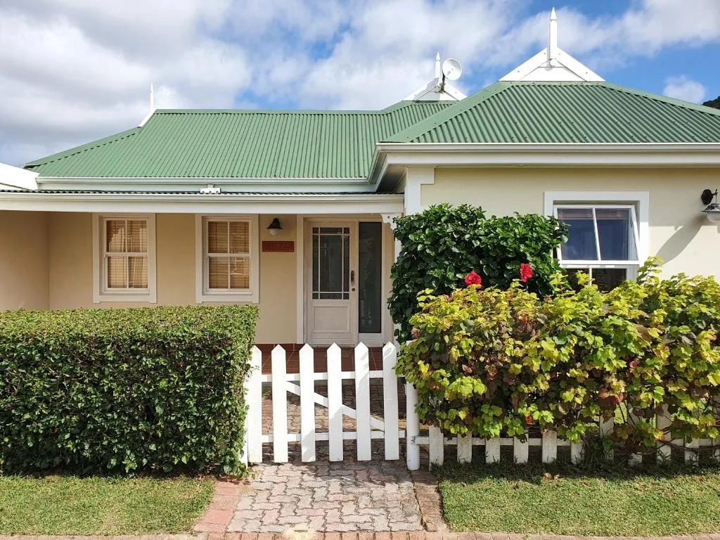 Cream cottage with green metal roof and white picket gate entrance