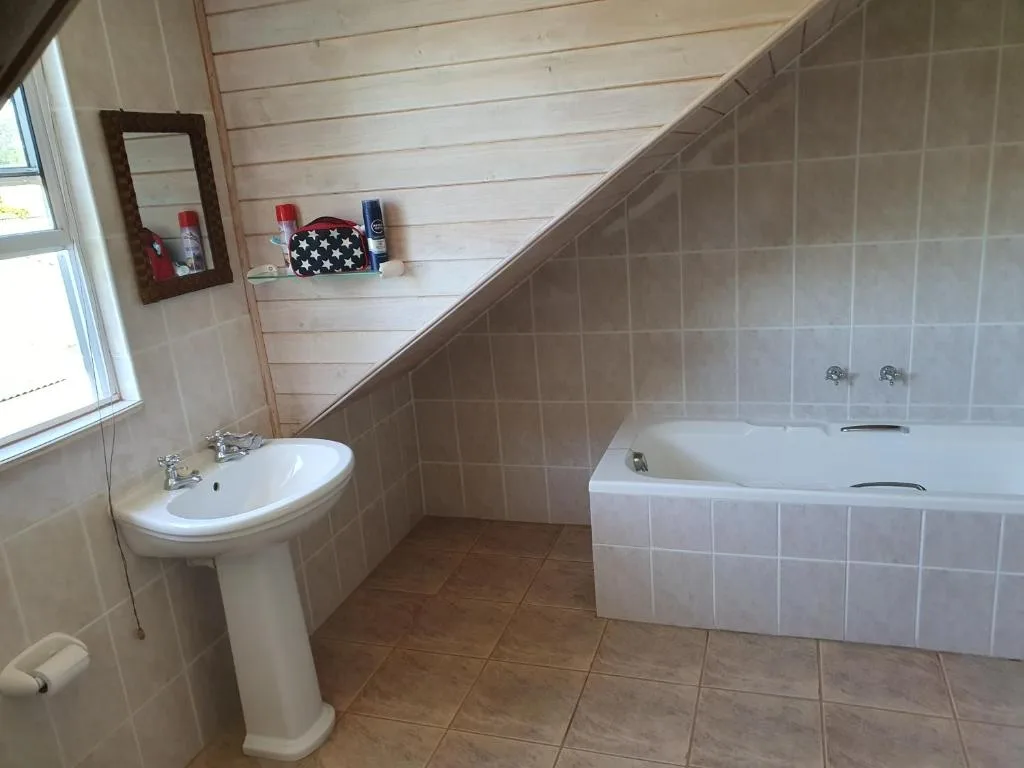 Spacious bathroom with pedestal sink and bathtub with tiled walls