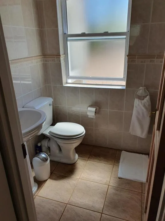 Small bathroom with toilet, window, tiled walls and beige flooring