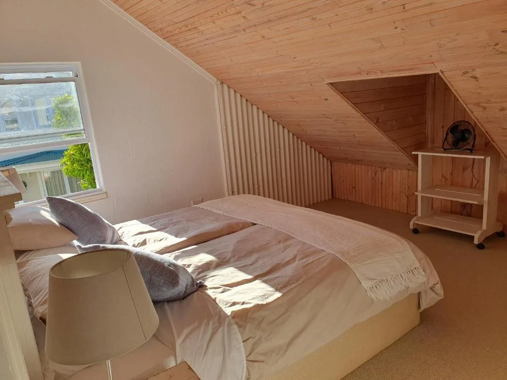Bright loft bedroom with double bed, wooden ceiling, and natural light from window