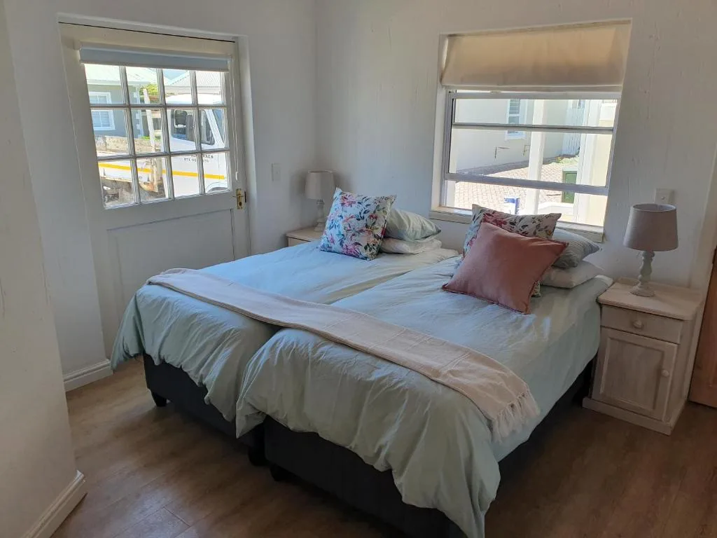 Bright bedroom with double bed, colorful pillows, wooden floors, and windows