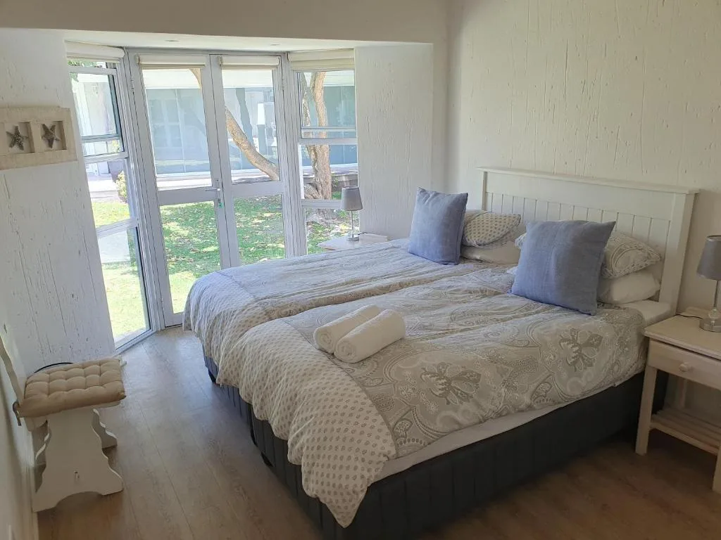 Bright bedroom with two beds, blue pillows, and glass doors overlooking garden