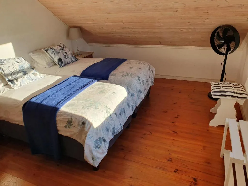Cozy attic bedroom with twin beds, wooden ceiling, and standing fan