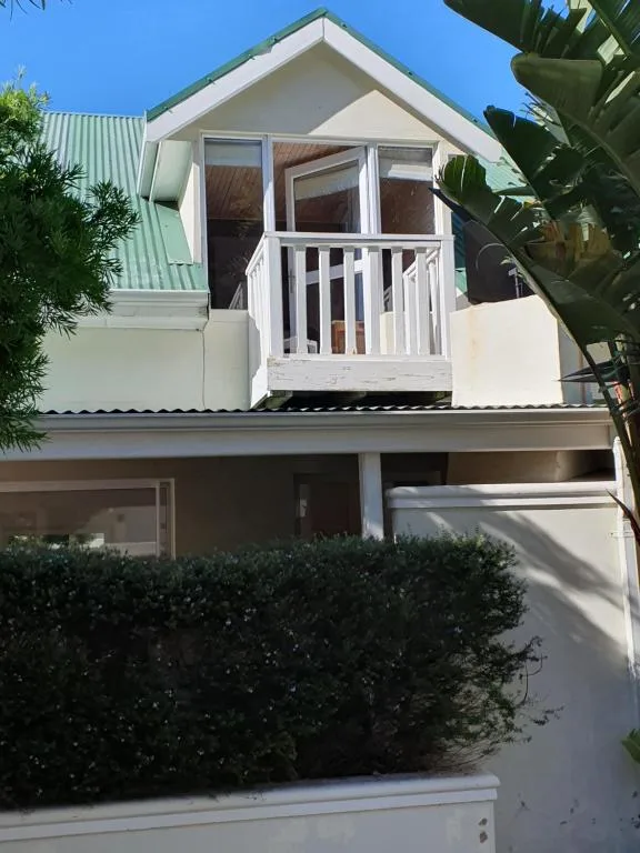 White villa with green roof and upper balcony, lush gardens and landscaping
