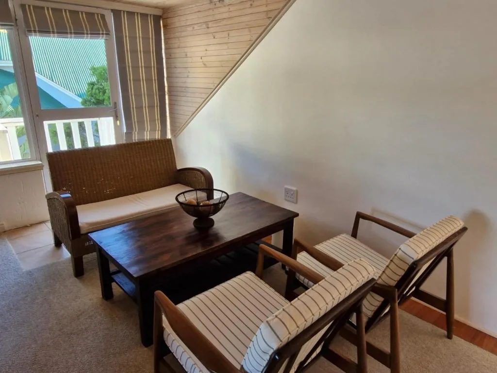 Spacious upstairs lounge with wicker sofa, dark wood coffee table, and striped chairs