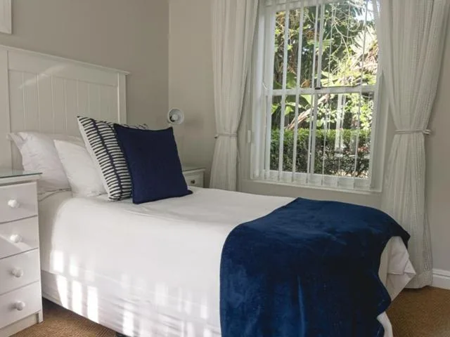 Bright bedroom with white bed, navy blanket, and large windows overlooking trees