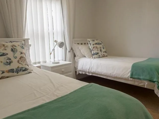 Twin bedroom with white bedding, green throws, and natural light from windows