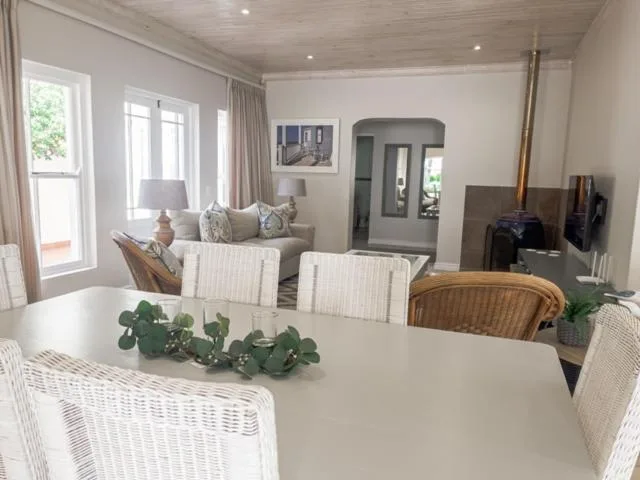 Bright dining area with white table, wicker chairs, and lounge seating visible beyond