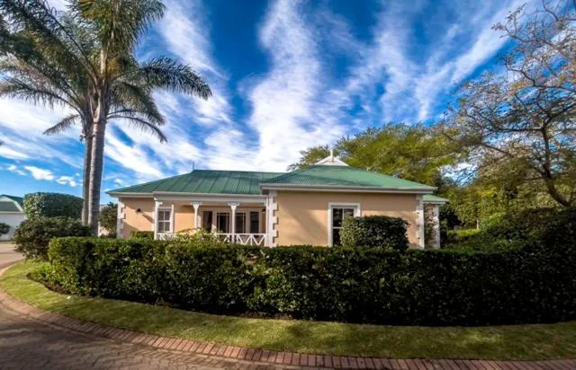 Cream-colored single-story home with green metal roof and manicured hedges