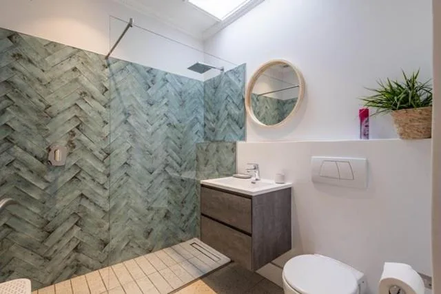 Modern bathroom with herringbone tile shower, vanity sink, and round mirror