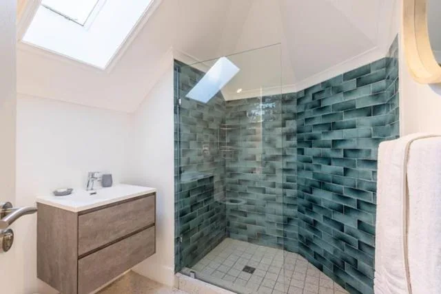 Modern bathroom with walk-in shower, green tiled walls, and wooden vanity