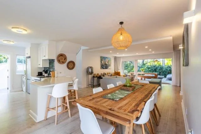 Open-plan dining area with wooden table and white chairs, kitchen visible