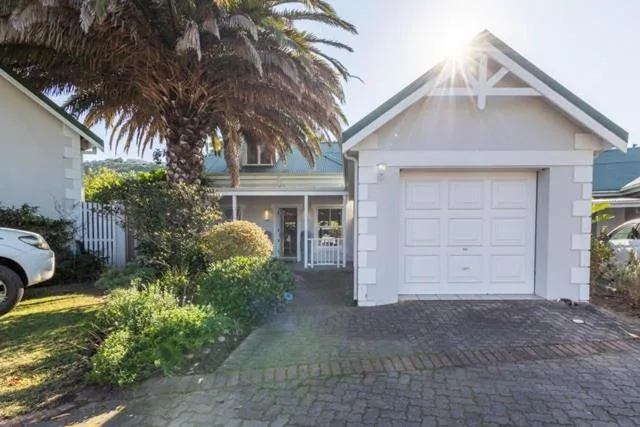 White cottage with garage, palm tree, and manicured garden frontage