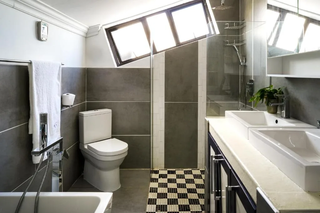 Modern bathroom with dark tile walls, walk-in shower, toilet, and double vanity sink