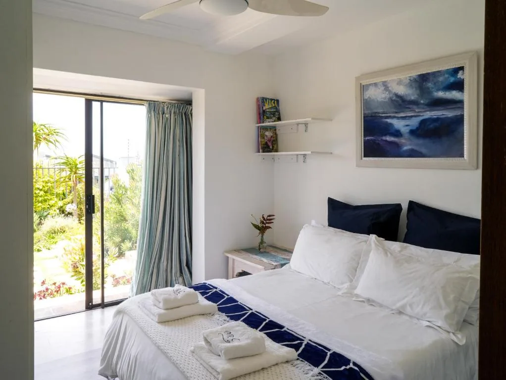 Bright bedroom with queen bed, ocean view artwork, and sliding doors to garden