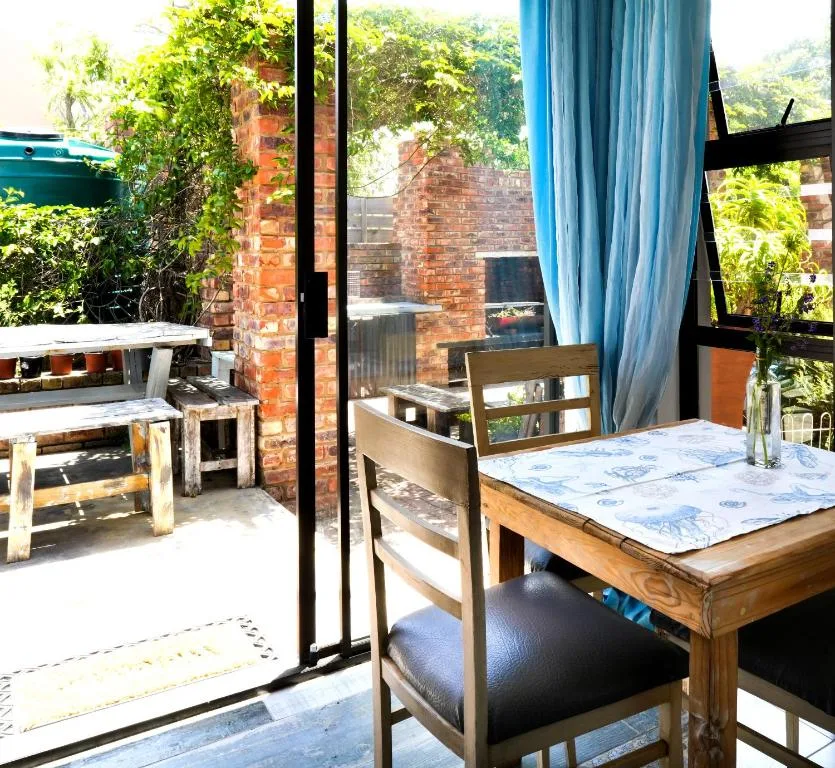 Outdoor patio with wooden dining table and brick braai area, lush greenery