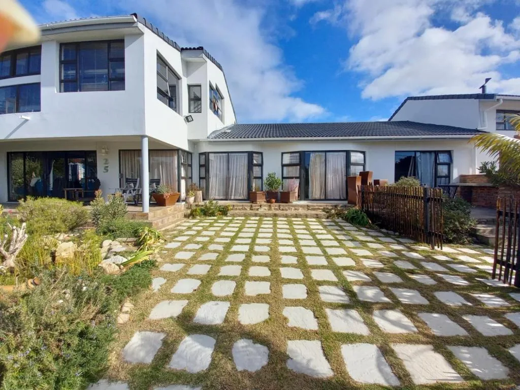 Modern white coastal home with geometric paving, native landscaping, and ocean views