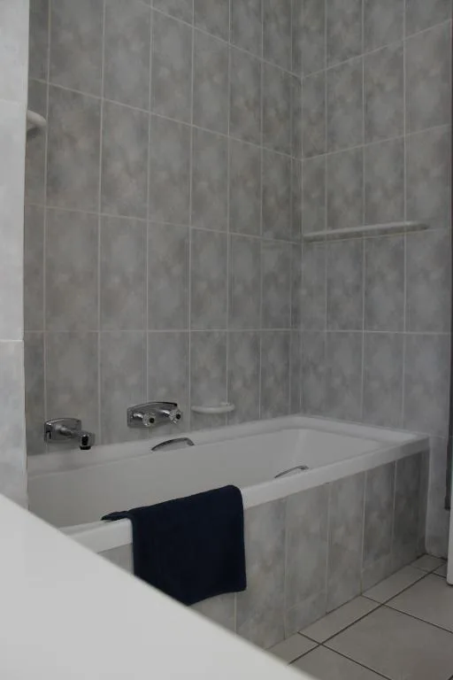 Modern bathroom with gray tiled walls and white bathtub with fixtures