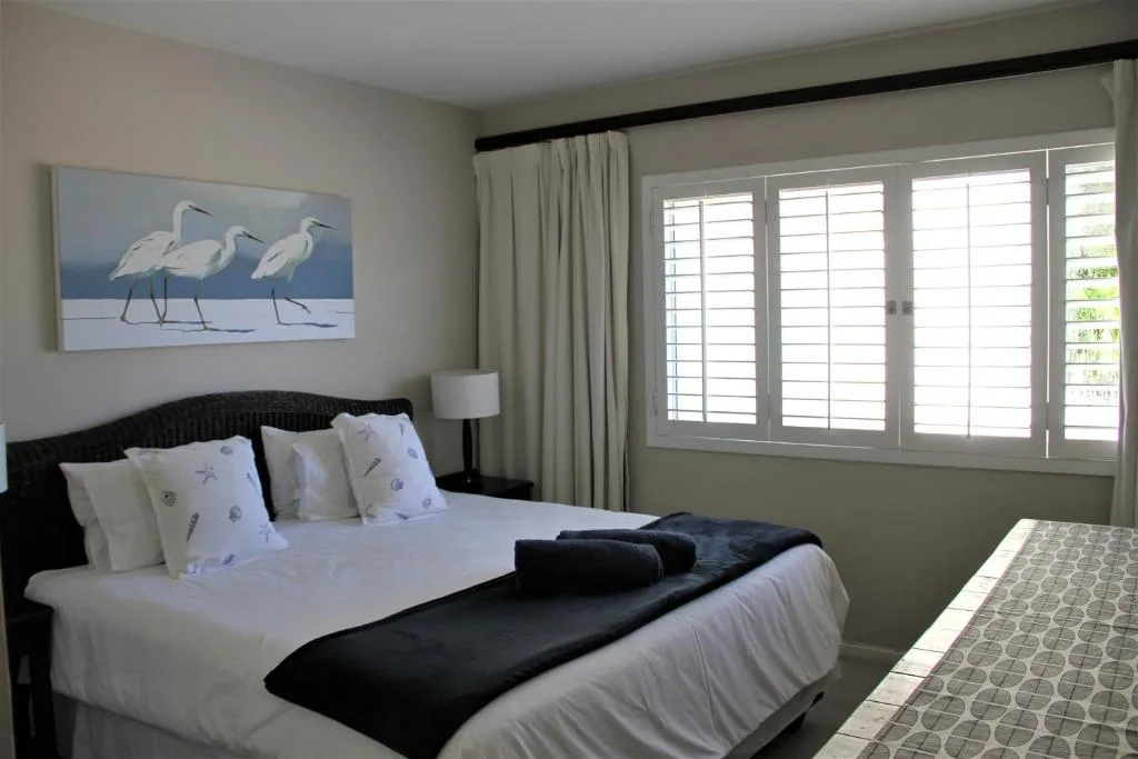 Bright bedroom with queen bed, coastal bird artwork, and white shuttered doors