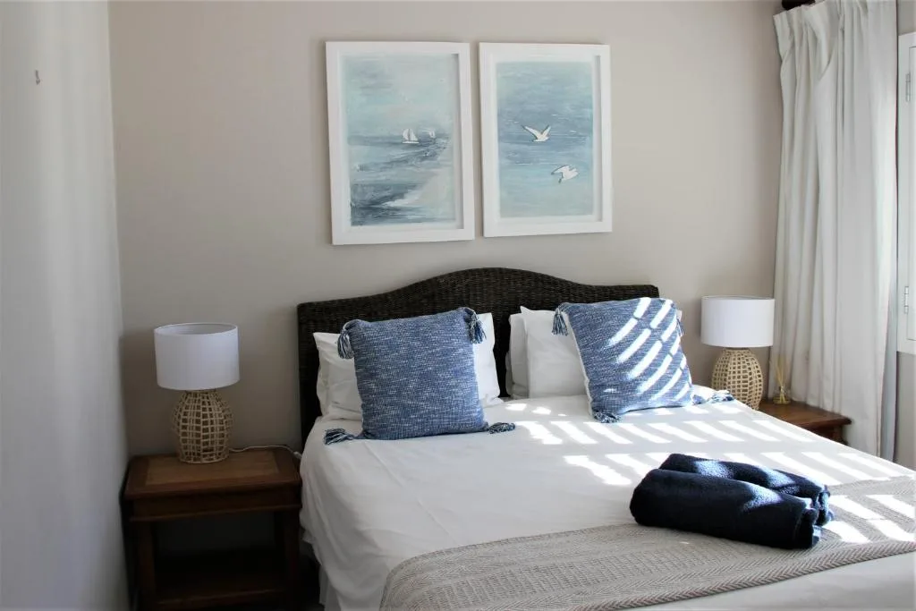Bright bedroom with white bed, blue striped pillows, nautical artwork above headboard