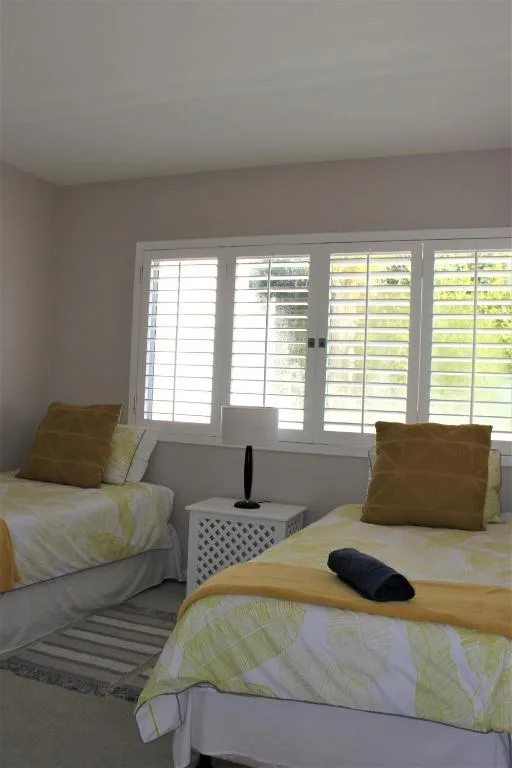 Bright bedroom with twin beds and plantation shutters overlooking garden