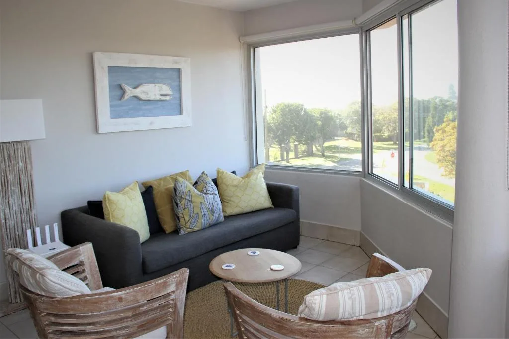 Comfortable lounge with dark sofa, armchairs, and scenic garden views through large windows