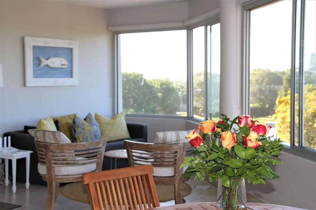 Bright lounge with black sofa, wooden chairs, and scenic forested views through large windows